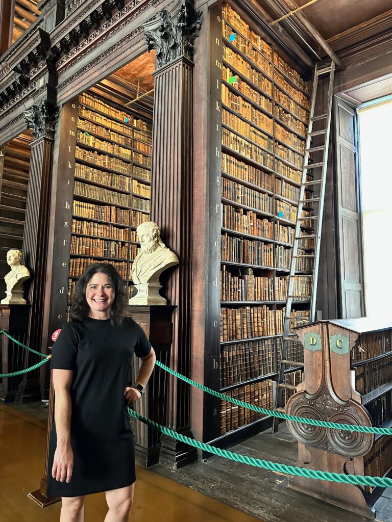 Kimberly, The Bougie Backpacker, standing in front of a section of books at Trinity Library in Dublin. 