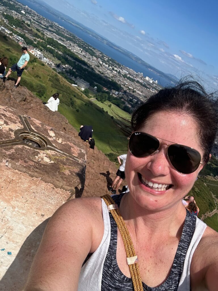 Kimberly taking a selfie next to a stone pillar that could be Arthurs Seat two